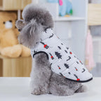 Side profile of a poodle wearing a white dog snow suit with red and black winter patterns
