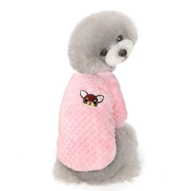 Grey fluffy dog wearing a pink dog face shirt with a cartoon dog patch on the back