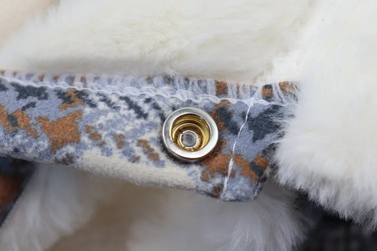 Close-up of a gold button detail on a blue plaid dog coat with white fleece lining