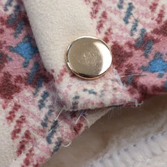 Close-up of the snap button detail on a pink plaid dog coat with white fleece lining