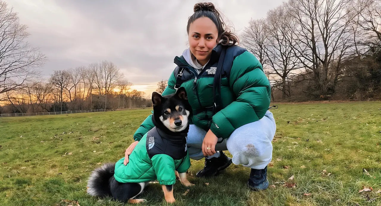 A woman and her dog wearing The Dog Face green jacket at sunset