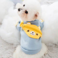 Small white dog wearing a light blue sweater with a yellow bear-shaped satchel, ideal Designer Dog Sweaters.