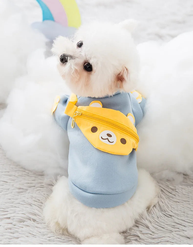 Small white dog wearing a light blue sweater with a yellow bear-shaped satchel, ideal Designer Dog Sweaters.