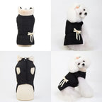A white poodle wearing a black fleece dog jacket with a cream-colored bow on the side, posing from the side and back views.