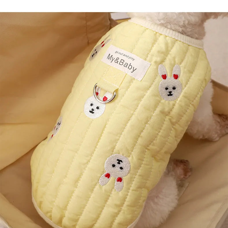 White poodle wearing a yellow embroidered dog sweatshirt with bunny design, back view.