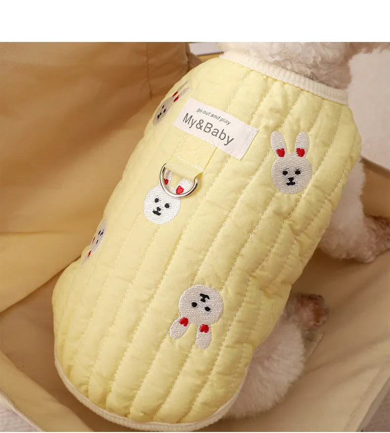 White poodle wearing a yellow embroidered dog sweatshirt with bunny design, back view.