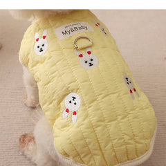 White poodle wearing a yellow embroidered dog sweatshirt with bunny design, back view.