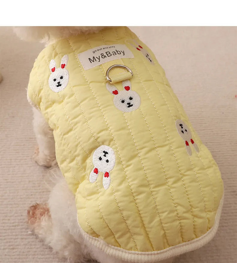 White poodle wearing a yellow embroidered dog sweatshirt with bunny design, back view.