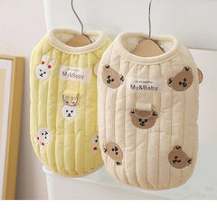 Two embroidered dog sweatshirts, one yellow with bunny design and one beige with bear design, hanging on a rack