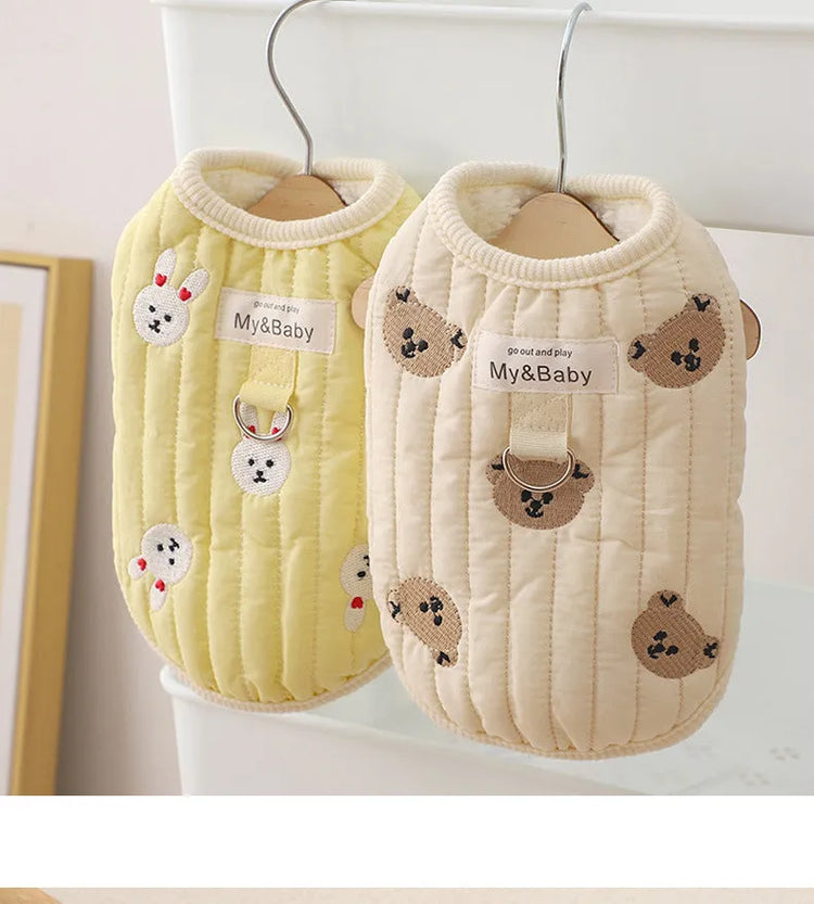 Two embroidered dog sweatshirts, one yellow with bunny design and one beige with bear design, hanging on a rack