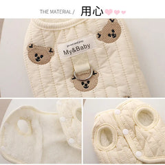 White poodle wearing an embroidered dog sweatshirt with bear design, standing and looking sideways."