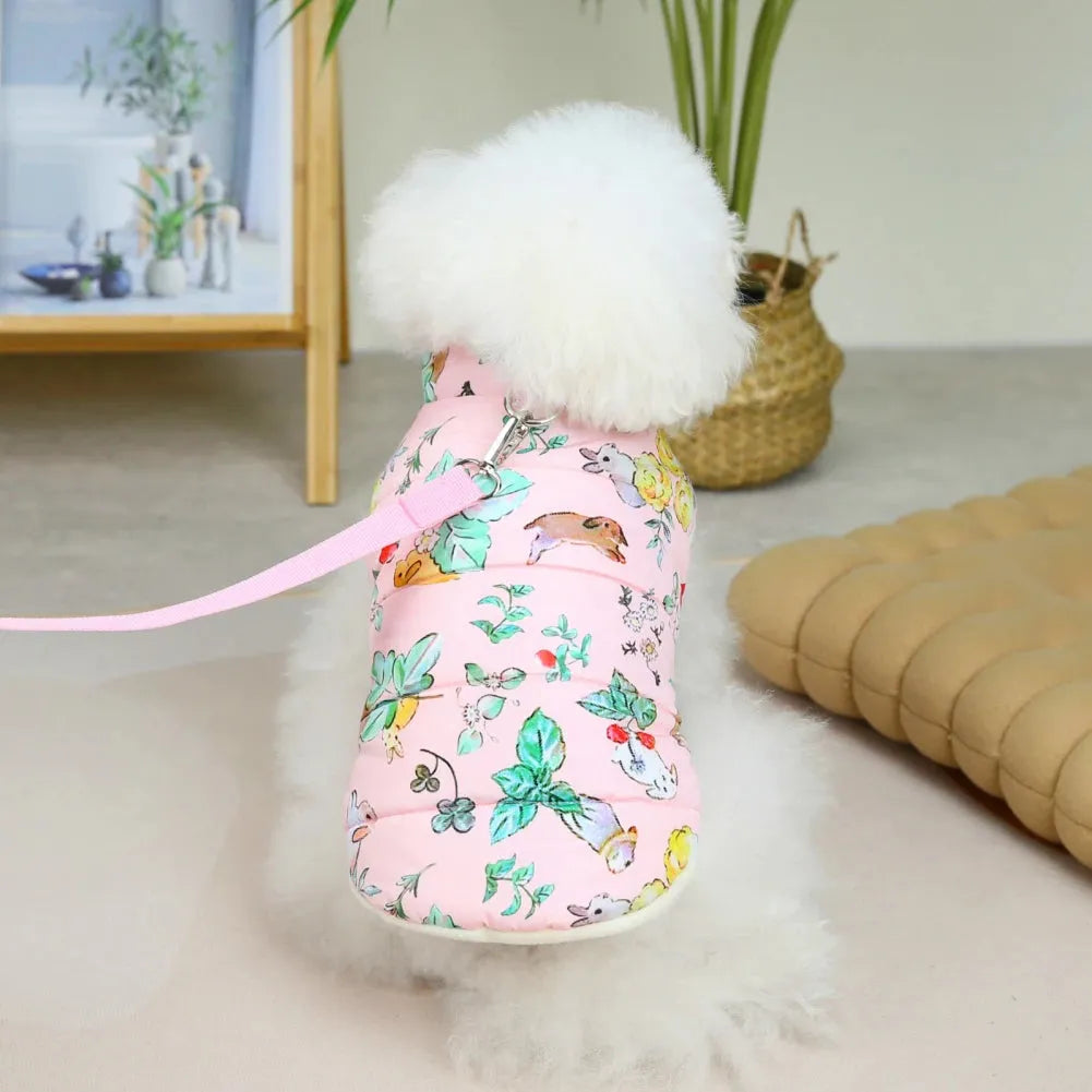 A white poodle wearing a pink dog coat with floral print, sitting and looking away.