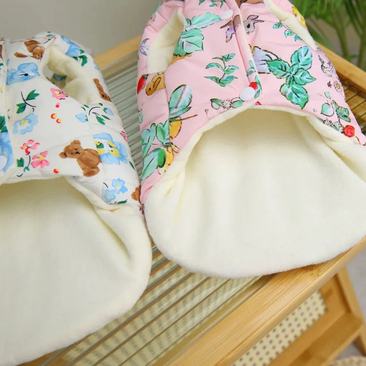 Close-up view of the inner lining of two dog coats, one white with floral and teddy bear print, and the other pink with floral print.