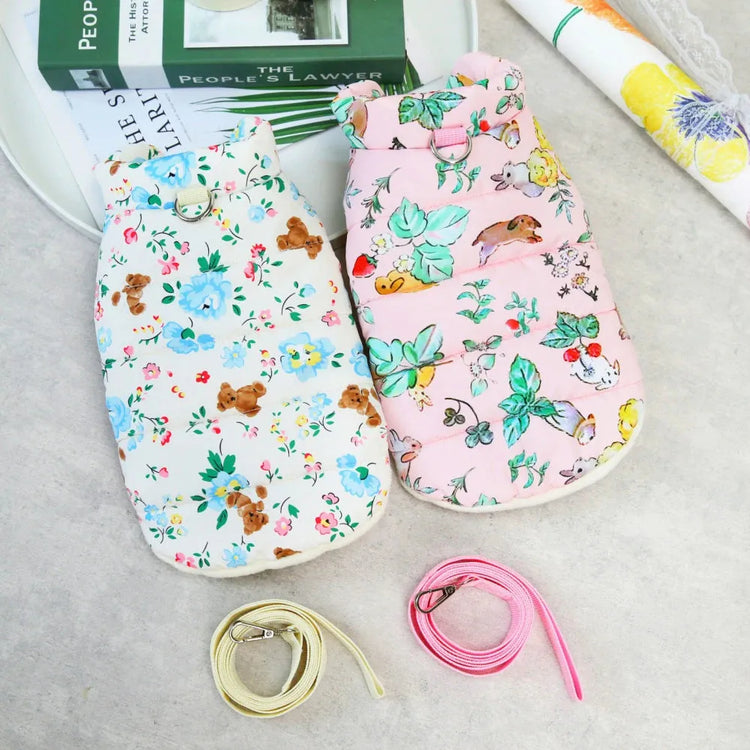 Two dog coats, one white with floral and teddy bear print, and the other pink with floral print, displayed with matching leashes.