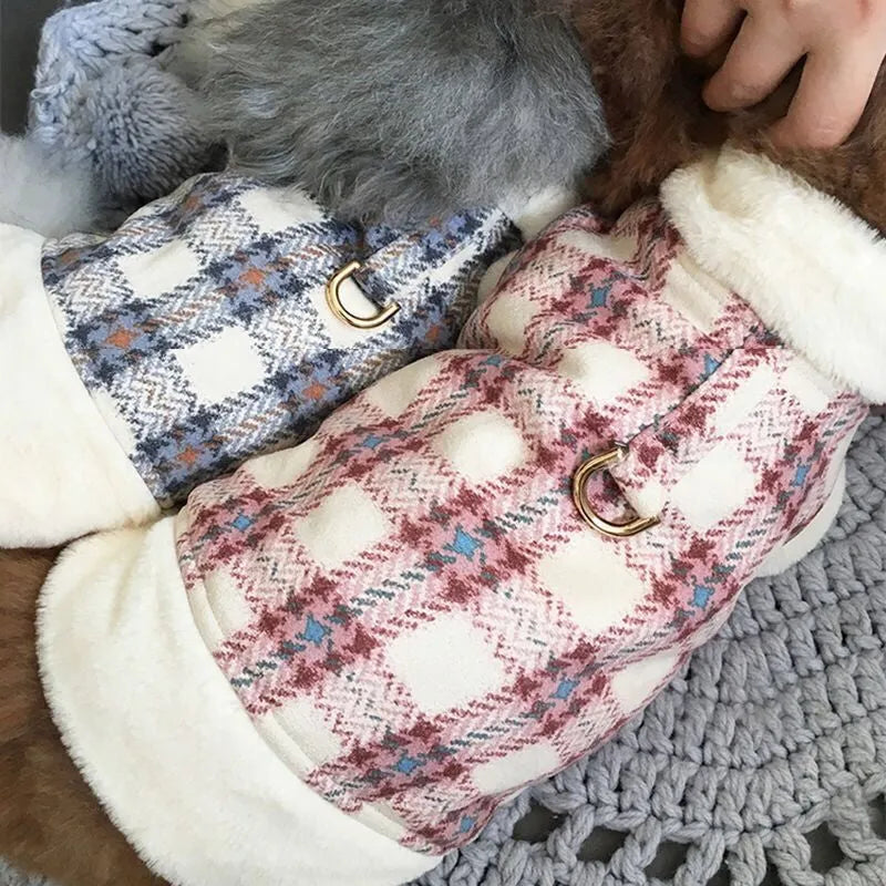 Two dogs wearing blue and pink plaid dog coats with fleece lining, lying on a knitted blanket